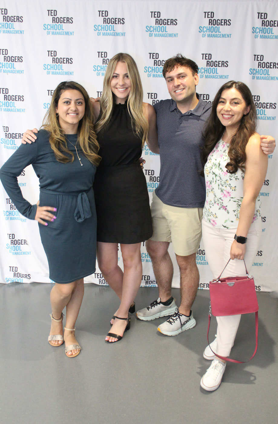 Four MScM alumni smiling and hugging and posing for the camera